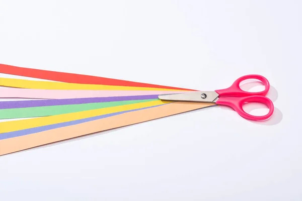 High angle view of scissors and colorful paper strips on white background — Stock Photo