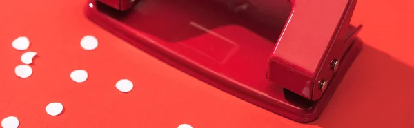 Tiro panorâmico de holepunch com círculos de papel no fundo vermelho — Fotografia de Stock