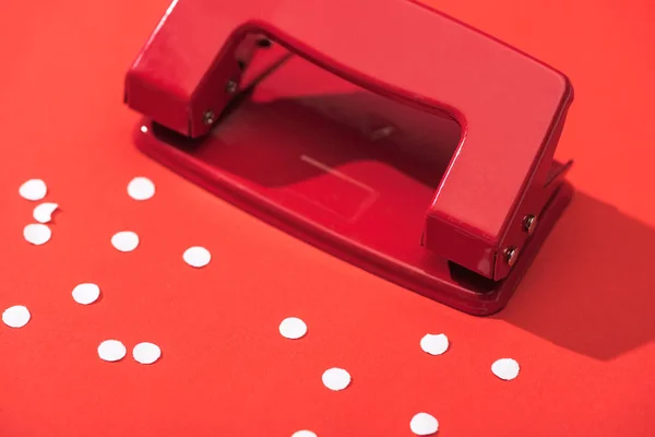 High angle view of holepunch with paper circles on red background — Stock Photo