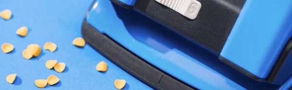 Panoramic shot of holepunch with paper circles on blue background — Stock Photo