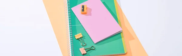 Plano panorámico de cuadernos, clips aglutinantes, sacapuntas y papel sobre fondo blanco - foto de stock