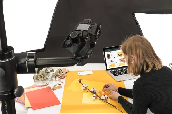 Fotógrafo haciendo composición con flor de algodón y accesorios para la toma de fotos con cámara y portátil - foto de stock
