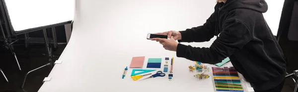 Cropped view of commercial photographer making photos of office supplies on smartphone, panoramic shot — Stock Photo