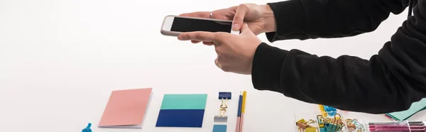 Cropped view of commercial photographer making photos of flat lay with office supplies on smartphone, panoramic shot — Stock Photo