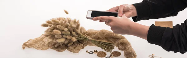 Partial view of commercial photographer taking pictures of composition with flora and jewelry on smartphone on white, panoramic shot — Stock Photo