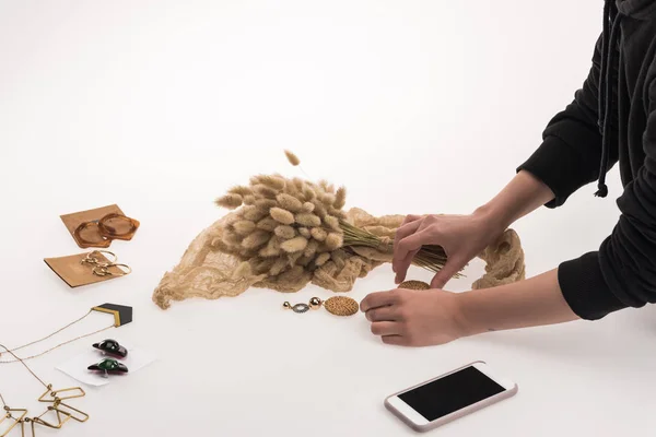 Partial view of commercial photographer making composition with flora and jewelry for commercial photography on smartphone on white — Stock Photo