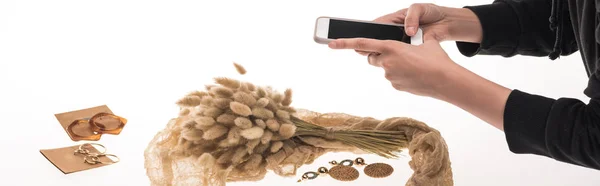 Partial view of commercial photographer taking pictures of composition with flora and jewelry on smartphone on white, panoramic shot — Stock Photo