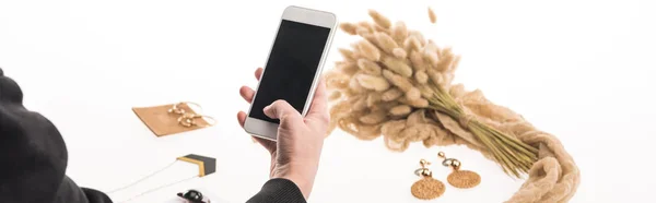 Cropped view of commercial photographer taking pictures of composition with flora and jewelry on smartphone on white, panoramic shot — Stock Photo