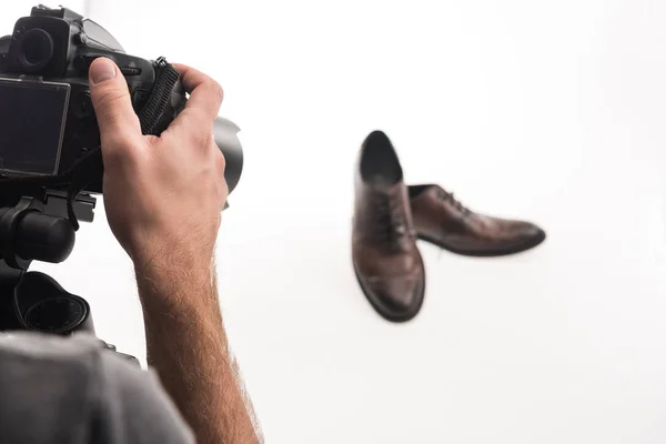 Vista recortada de fotógrafo masculino haciendo sesión de fotos comerciales de zapatos masculinos en blanco - foto de stock
