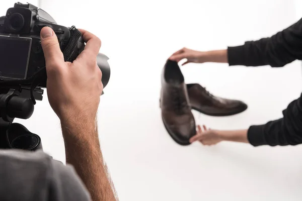 Vista recortada de fotógrafos comerciales haciendo sesión de fotos de zapatos masculinos en blanco - foto de stock