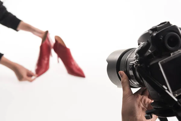 Vista recortada de fotógrafos comerciales haciendo sesión de fotos comerciales de zapatos de tacón rojo femenino en blanco - foto de stock