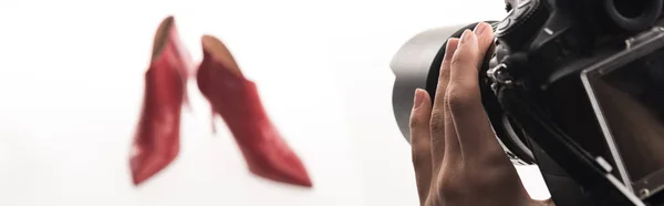 Vista recortada del fotógrafo haciendo sesión de fotos comerciales de zapatos de tacón rojo femenino en blanco, tiro panorámico - foto de stock