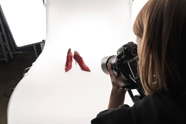 Abgeschnittene Ansicht des kommerziellen Fotografen, der kommerzielle Fotoshootings von weiblichen roten Fersenschuhen auf Weiß macht — Stockfoto