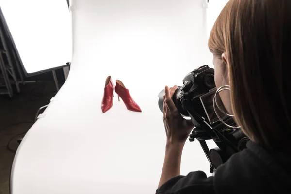 Photographe faisant séance photo commerciale de chaussures à talons rouges féminines sur blanc — Photo de stock