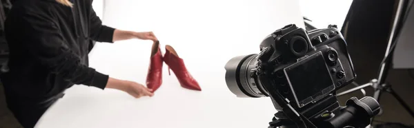 Vista cortada de fotógrafo comercial fazendo sessão de fotos comerciais de sapatos femininos de salto vermelho em branco, tiro panorâmico — Fotografia de Stock