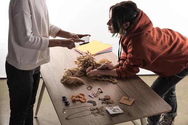 Two commercial photographers taking pictures of composition with flora and accessories on smartphone — Stock Photo