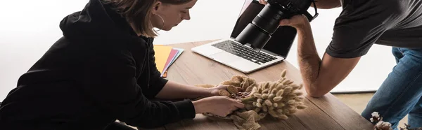 Vista recortada de dos fotógrafos comerciales tomar una foto de la composición con flora y accesorios en la cámara digital - foto de stock