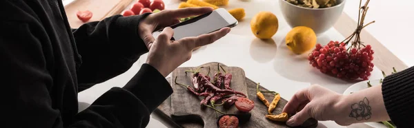 Vista recortada de dos fotógrafos profesionales haciendo la composición de alimentos para la fotografía comercial en el teléfono inteligente en la mesa de madera - foto de stock