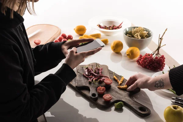 Vista recortada de dos fotógrafos haciendo composición de alimentos para la fotografía comercial en el teléfono inteligente en la mesa de madera - foto de stock