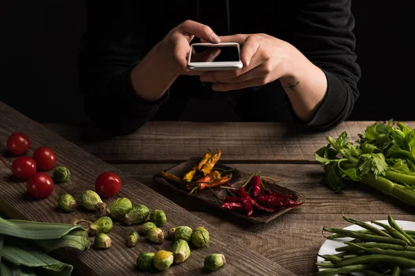 Visão recortada de fotógrafo profissional fazendo composição de alimentos para fotografia comercial em smartphone na mesa de madeira — Fotografia de Stock