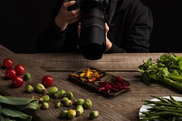 Vista recortada de fotógrafa haciendo composición de alimentos para fotografía comercial y tomando fotos en cámara digital en mesa de madera - foto de stock