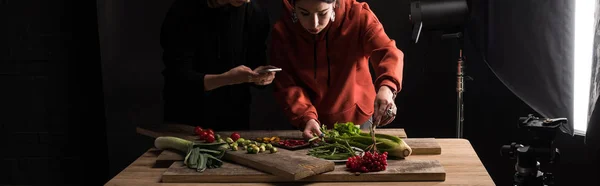 Vista recortada de dois fotógrafos que fazem composição de alimentos para fotografia comercial em smartphone, tiro panorâmico — Fotografia de Stock