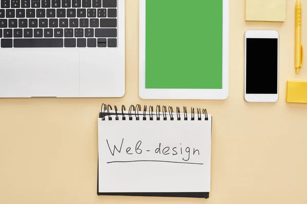 Flat lay com gadgets e letras web design no bloco de notas em fundo amarelo — Fotografia de Stock