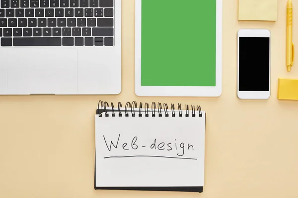 Posa piatta con gadget e lettering web design in blocco note su sfondo giallo — Foto stock