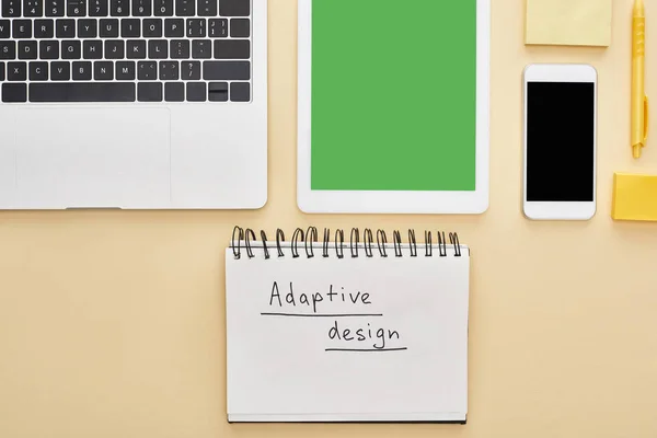 Posa piatta con gadget e scritte di design adattivo in blocco note su sfondo giallo — Foto stock