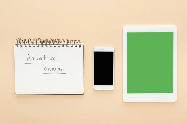 Flat lay with gadgets near notebook with adaptive design lettering on beige background — Stock Photo