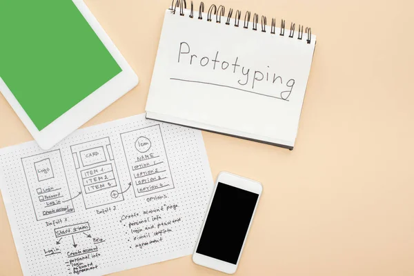 Draufsicht auf Gadgets in der Nähe von Website-Design-Vorlage und Notizbuch mit Prototyping-Schriftzug auf beigem Hintergrund — Stockfoto
