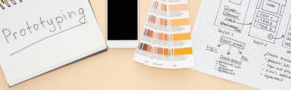 Vista superior del teléfono inteligente cerca de la plantilla de diseño del sitio web, paleta de colores y portátil con letras de prototipado sobre fondo beige, plano panorámico - foto de stock