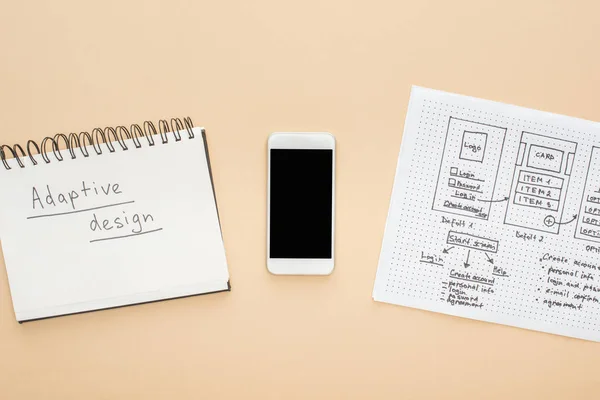 Vista dall'alto dello smartphone vicino al modello di design del sito web e notebook con scritte di design adattivo su sfondo beige — Foto stock