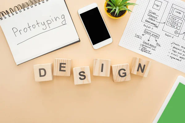 Draufsicht auf Gadgets in der Nähe von Holzblöcken mit Design-Schriftzug, Website-Design-Vorlage, Notizbuch mit Prototyping-Schriftzug und grüner Pflanze auf beigem Hintergrund — Stockfoto