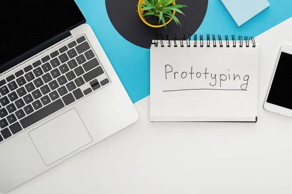 Vista superior de laptop, smartphone, planta, notebook com prototipagem lettering em fundo geométrico abstrato — Fotografia de Stock