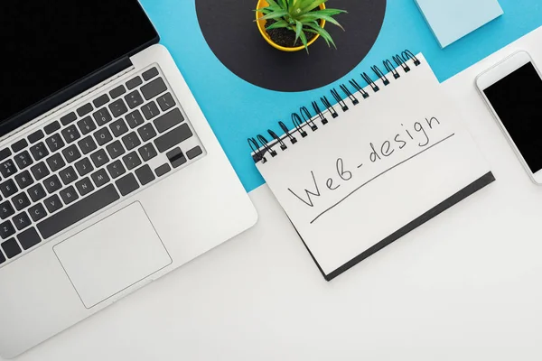 Vista superior de laptop, smartphone, planta, notebook com letras web design em fundo geométrico abstrato — Fotografia de Stock