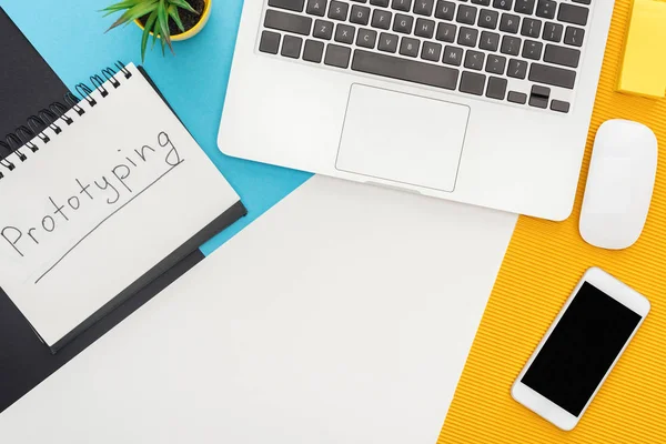 Vista dall'alto di blocco note con prototipazione lettering, laptop, mouse, smartphone, impianto su sfondo geometrico astratto — Foto stock