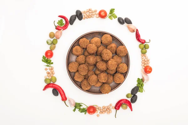 Blick von oben auf Kichererbsen, Knoblauch, Kirschtomaten, Petersilie, Oliven, Chilischote, grüne Zwiebeln in rundem Rahmen um Falafel-Bällchen auf Teller isoliert auf weiß angeordnet — Stockfoto