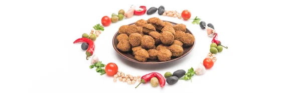 Chickpea, garlic, cherry tomatoes, parsley, olives, chili pepper, green onion arranged in round frame around falafel balls on plate on white background, panoramic shot — Stock Photo