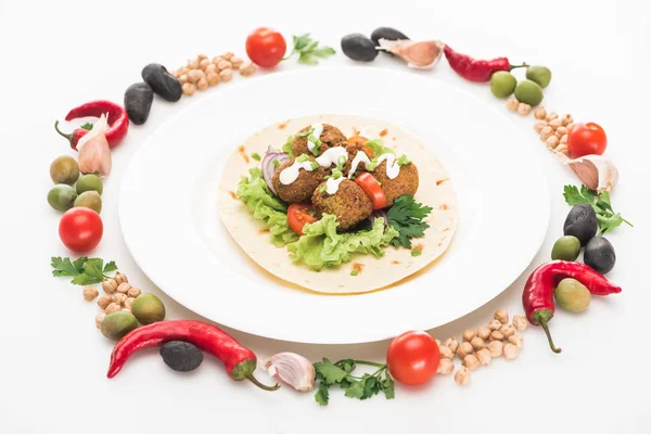 Vegetables arranged in round frame around falafel on pita on plate on white background — Stock Photo