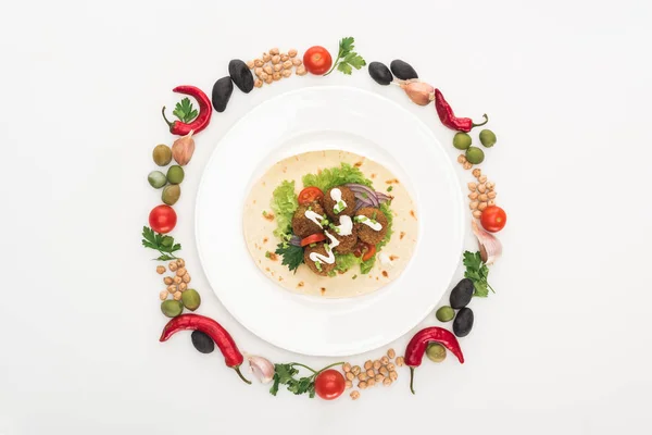 Vista dall'alto di verdure disposte in cornice rotonda intorno a falafel su pita su piatto su sfondo bianco — Foto stock