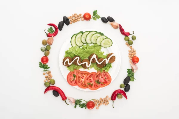 Top view of vegetables arranged in round frame around falafel with sauce on plate on white background — Stock Photo