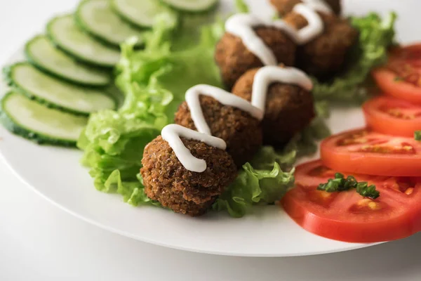 Primer plano vista de falafel con salsa en el plato con verduras en rodajas sobre fondo blanco - foto de stock