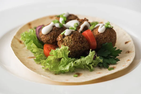 Vista de perto de falafel com molho em pita com legumes em placa branca — Fotografia de Stock