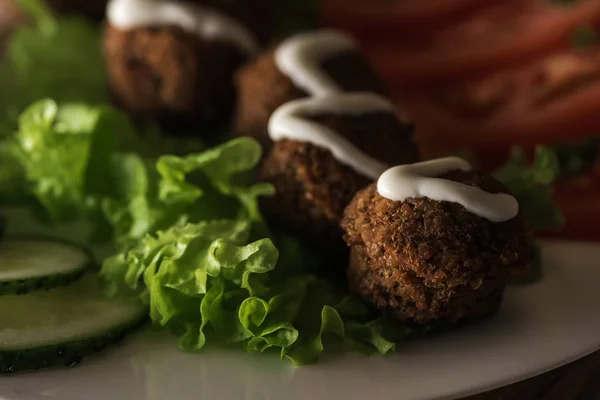 Primer plano vista de falafel con salsa en el plato con verduras en rodajas en oscuro, plano panorámico - foto de stock