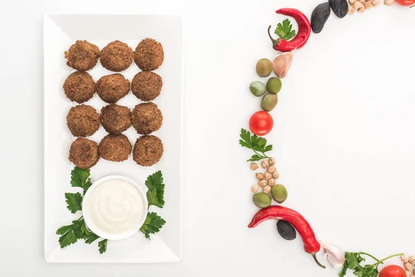 Vista superior de legumes dispostos em armação redonda perto de falafel na placa com molho no fundo branco — Fotografia de Stock