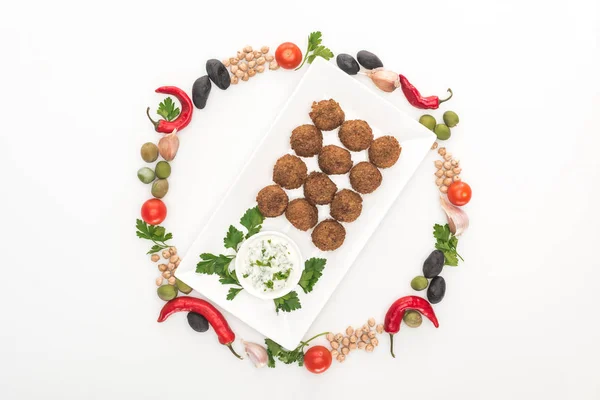 Vista dall'alto di verdure disposte in cornice rotonda intorno a falafel su piatto con salsa su sfondo bianco — Foto stock