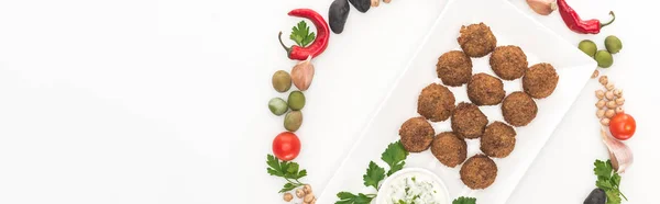 Draufsicht auf Gemüse in rundem Rahmen um Falafel auf Teller mit Soße auf weißem Hintergrund angeordnet, Panoramaaufnahme — Stockfoto