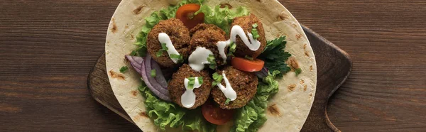 Vista dall'alto del falafel con verdure e salsa sulla pita sul tavolo di legno, colpo panoramico — Foto stock