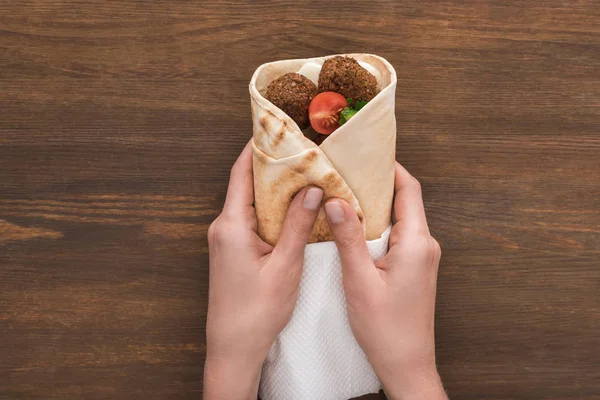 Vista ritagliata di donna che tiene falafel con verdure e salsa in pita sul tavolo di legno — Foto stock